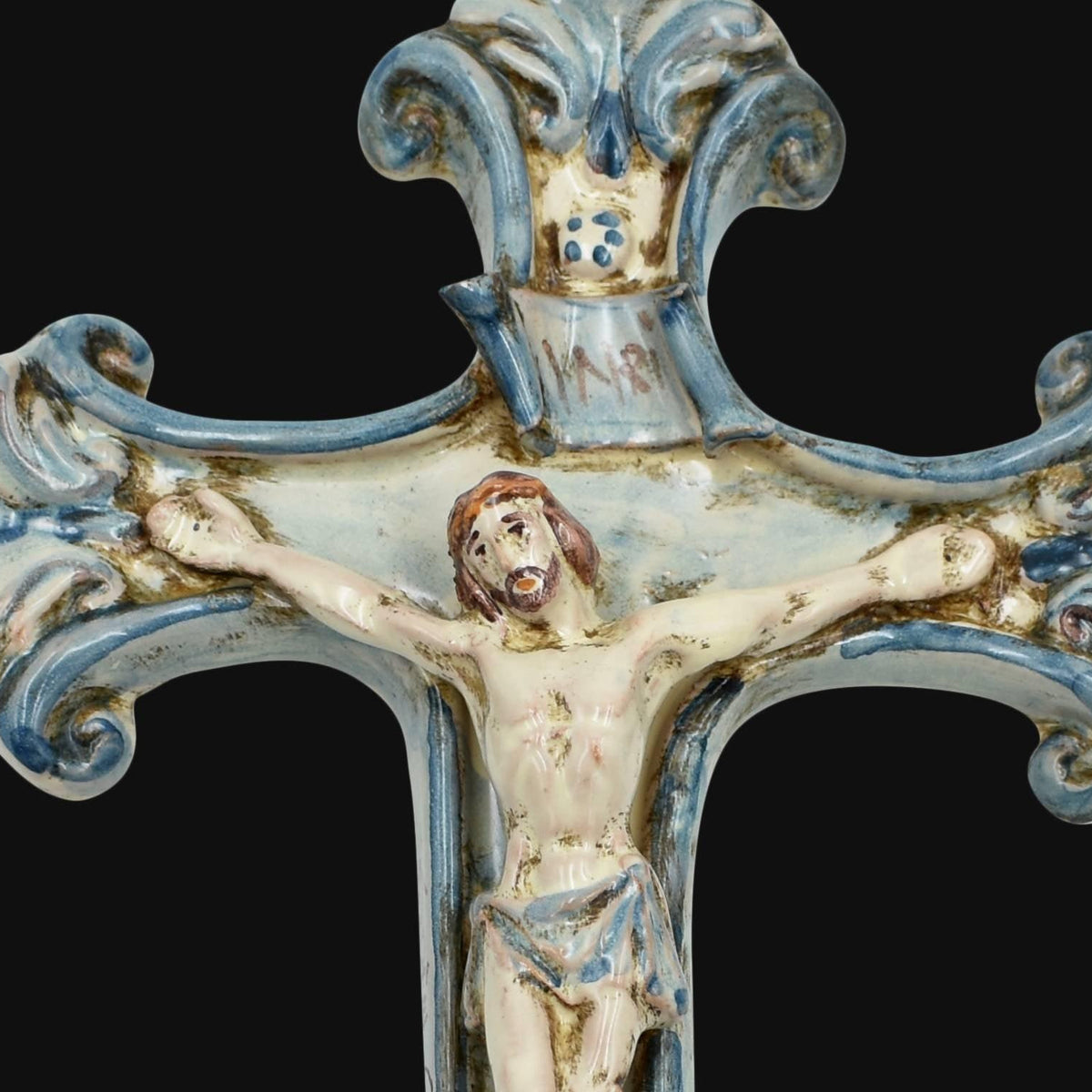 Dettaglio del crocifisso in ceramica di Caltagirone Mono Blu: Cristo in rilievo, cartiglio INRI e cimasa a volute dipinte a mano in blu