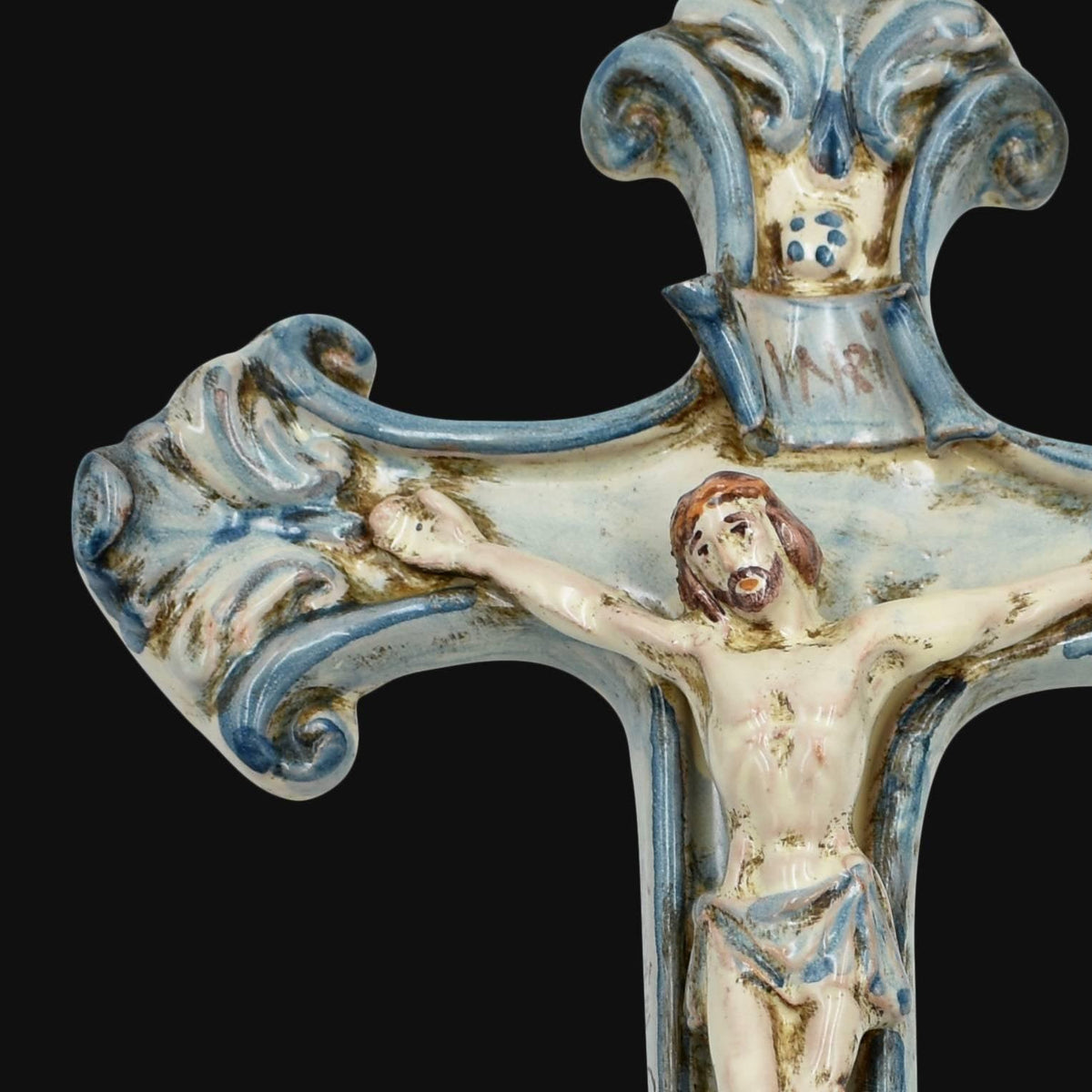 Dettaglio del braccio sinistro del crocifisso in ceramica di Caltagirone Mono Blu, con volute in rilievo dipinte a mano in blu e la figura del Cristo