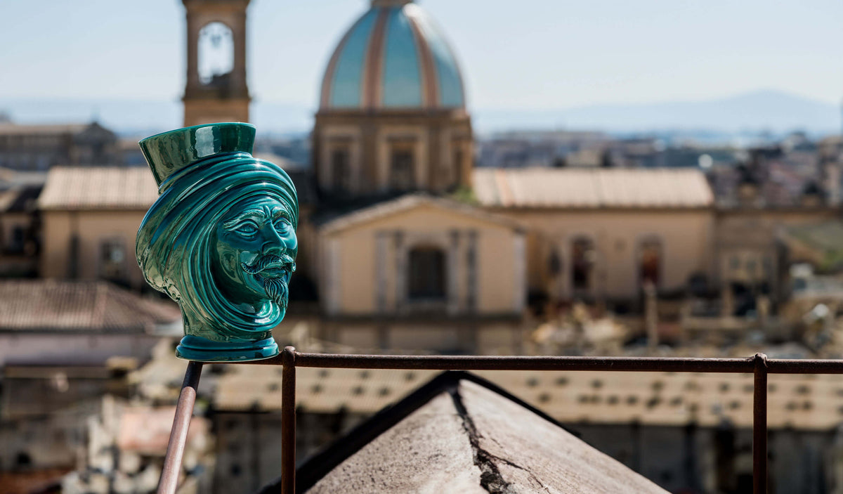 Testa di moro in ceramica di Caltagirone fatta a mano, colore turchese, su balcone con panorama città